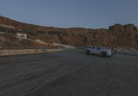 two cars are parked on the road in front of a mountain and ocean shore resort