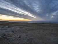 a lone bench is near the ocean during sunset, with an open sky behind it