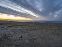 a lone bench is near the ocean during sunset, with an open sky behind it