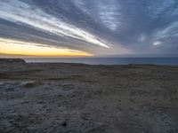 a lone bench is near the ocean during sunset, with an open sky behind it