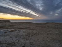 a lone bench is near the ocean during sunset, with an open sky behind it