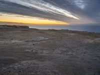 a lone bench is near the ocean during sunset, with an open sky behind it