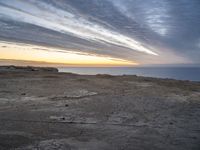 a lone bench is near the ocean during sunset, with an open sky behind it