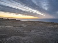 a lone bench is near the ocean during sunset, with an open sky behind it