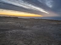 a lone bench is near the ocean during sunset, with an open sky behind it