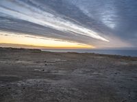 a lone bench is near the ocean during sunset, with an open sky behind it