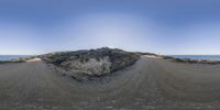 this is a fish eye view of some dirt road and mountains in the distance to the left and the sky to the right of the hill