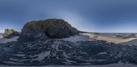 a fish - eye view of some very large rocks on the beach with a small area of sand on the ocean