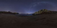 the milky shines brightly in the night sky as seen from a rocky coastline on a dark beach