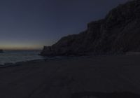 an empty street near some rocks by the sea at night with the sun setting over the water