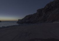 an empty street near some rocks by the sea at night with the sun setting over the water