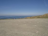 a parking lot that has only two people on it next to the ocean, with a few people walking in front of it