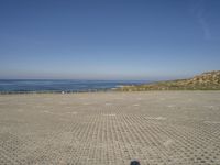 a parking lot that has only two people on it next to the ocean, with a few people walking in front of it