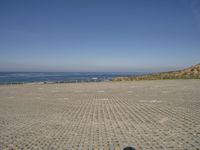 a parking lot that has only two people on it next to the ocean, with a few people walking in front of it