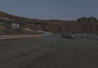 a truck drives along the side of the road near a cliff with houses, cars and mountain in the background