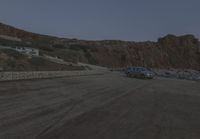 a truck drives along the side of the road near a cliff with houses, cars and mountain in the background