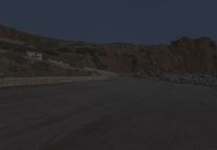 a truck drives along the side of the road near a cliff with houses, cars and mountain in the background