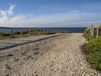 a dirt path next to the ocean near a beach with a bench that overlooks the water