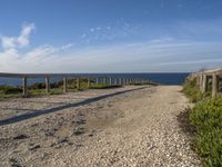 a dirt path next to the ocean near a beach with a bench that overlooks the water