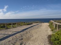 a dirt path next to the ocean near a beach with a bench that overlooks the water