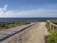 a dirt path next to the ocean near a beach with a bench that overlooks the water