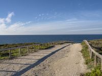 a dirt path next to the ocean near a beach with a bench that overlooks the water