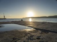 an orange sun shines in a blue puddle on the beach at low tide, and the water has reflectioning