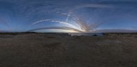 a very large curved object in the sky over a desert plain, and people walking in it