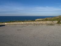 an asphalt parking lot with blue skies and the ocean in the background with two people on skateboards near the top