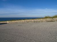 an asphalt parking lot with blue skies and the ocean in the background with two people on skateboards near the top