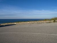 an asphalt parking lot with blue skies and the ocean in the background with two people on skateboards near the top