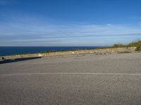 an asphalt parking lot with blue skies and the ocean in the background with two people on skateboards near the top