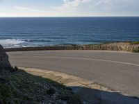 a view of the ocean with the curved road beside it, and to the left of the road is the coastline and to the right