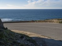 a view of the ocean with the curved road beside it, and to the left of the road is the coastline and to the right