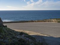 a view of the ocean with the curved road beside it, and to the left of the road is the coastline and to the right