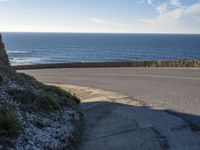 a view of the ocean with the curved road beside it, and to the left of the road is the coastline and to the right