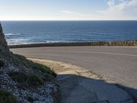 a view of the ocean with the curved road beside it, and to the left of the road is the coastline and to the right