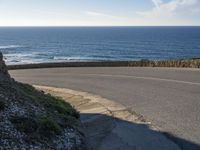 a view of the ocean with the curved road beside it, and to the left of the road is the coastline and to the right