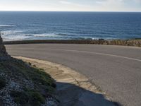 a view of the ocean with the curved road beside it, and to the left of the road is the coastline and to the right