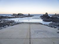 a view across the concrete ground at some water and rocks in the distance with an open door leading into a beach