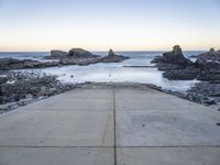 a view across the concrete ground at some water and rocks in the distance with an open door leading into a beach