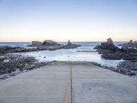 a view across the concrete ground at some water and rocks in the distance with an open door leading into a beach