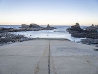 a view across the concrete ground at some water and rocks in the distance with an open door leading into a beach