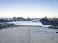 a view across the concrete ground at some water and rocks in the distance with an open door leading into a beach