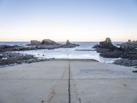 a view across the concrete ground at some water and rocks in the distance with an open door leading into a beach