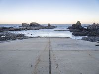 a view across the concrete ground at some water and rocks in the distance with an open door leading into a beach