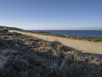 a man riding a motorcycle down the side of a dirt road next to an ocean