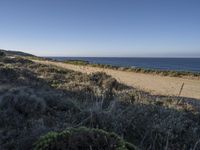 a man riding a motorcycle down the side of a dirt road next to an ocean