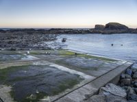 a fire hydrant next to the ocean with rocks and water surrounding it with boats on the water