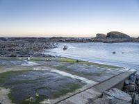 a fire hydrant next to the ocean with rocks and water surrounding it with boats on the water